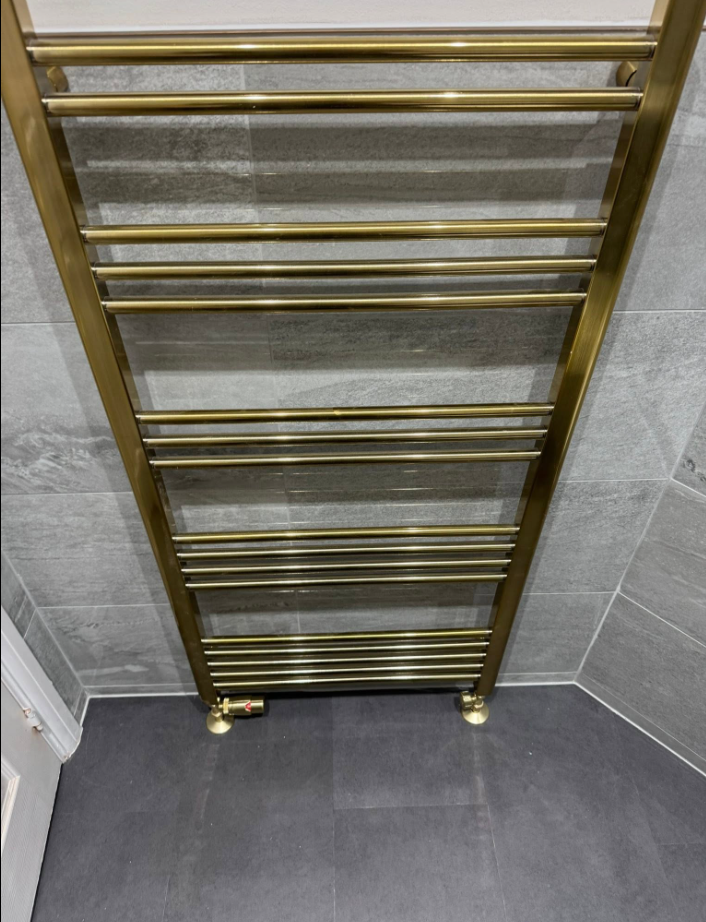 Brushed brass heated towel rail fitted and plumbed in a grey tiled bathroom