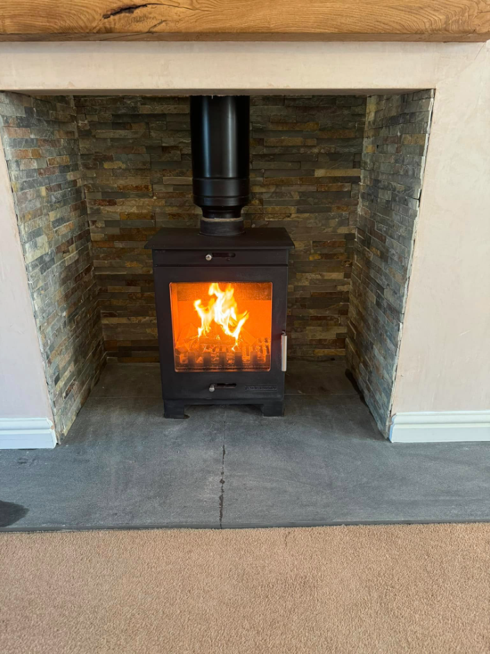 Log burner installed in a split-face stone chamber with oak beam mantel